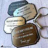 Four personalized horse stall warning signs in brushed metallic finishes displayed with an equestrian horse bit, showing different colors and messages.