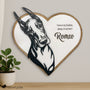 A heart-shaped wooden plaque featuring a black metal portrait of a Doberman and the engraved name "Romeo" with the phrase "Forever my shadow, always in my heart" is displayed on a light wall above a wooden surface. A small potted plant and soft lighting add warmth to the scene. The Fido & Flicka logo appears in the bottom left corner.