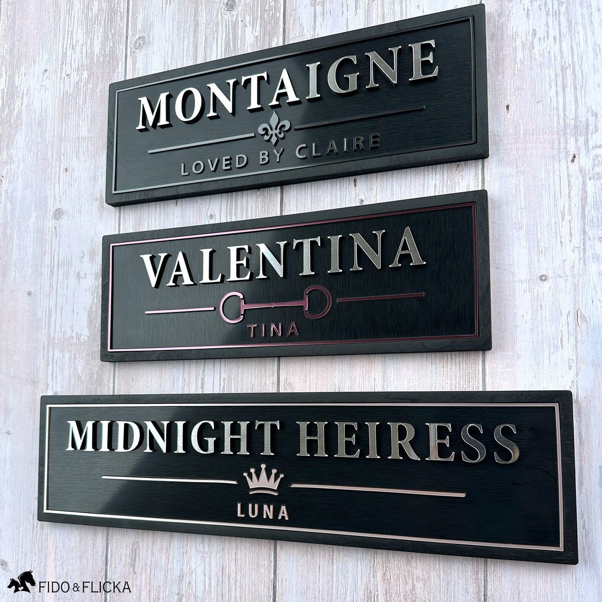 Three luxury personalized horse stall name plates shown in Graphite, Merlot, and Rosé Champagne metallic finishes with custom horse names and emblems.
