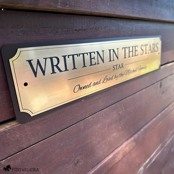 Personalized brushed gold horse stall sign mounted on a wooden barn wall with engraved horse name, barn name, and owner personalization.