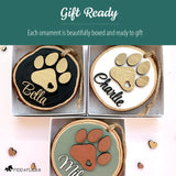 Three personalized dog paw wood slice ornaments—black, white, and sage—shown packaged in gift boxes, highlighting the gift-ready presentation and layered wooden paw prints with custom names.