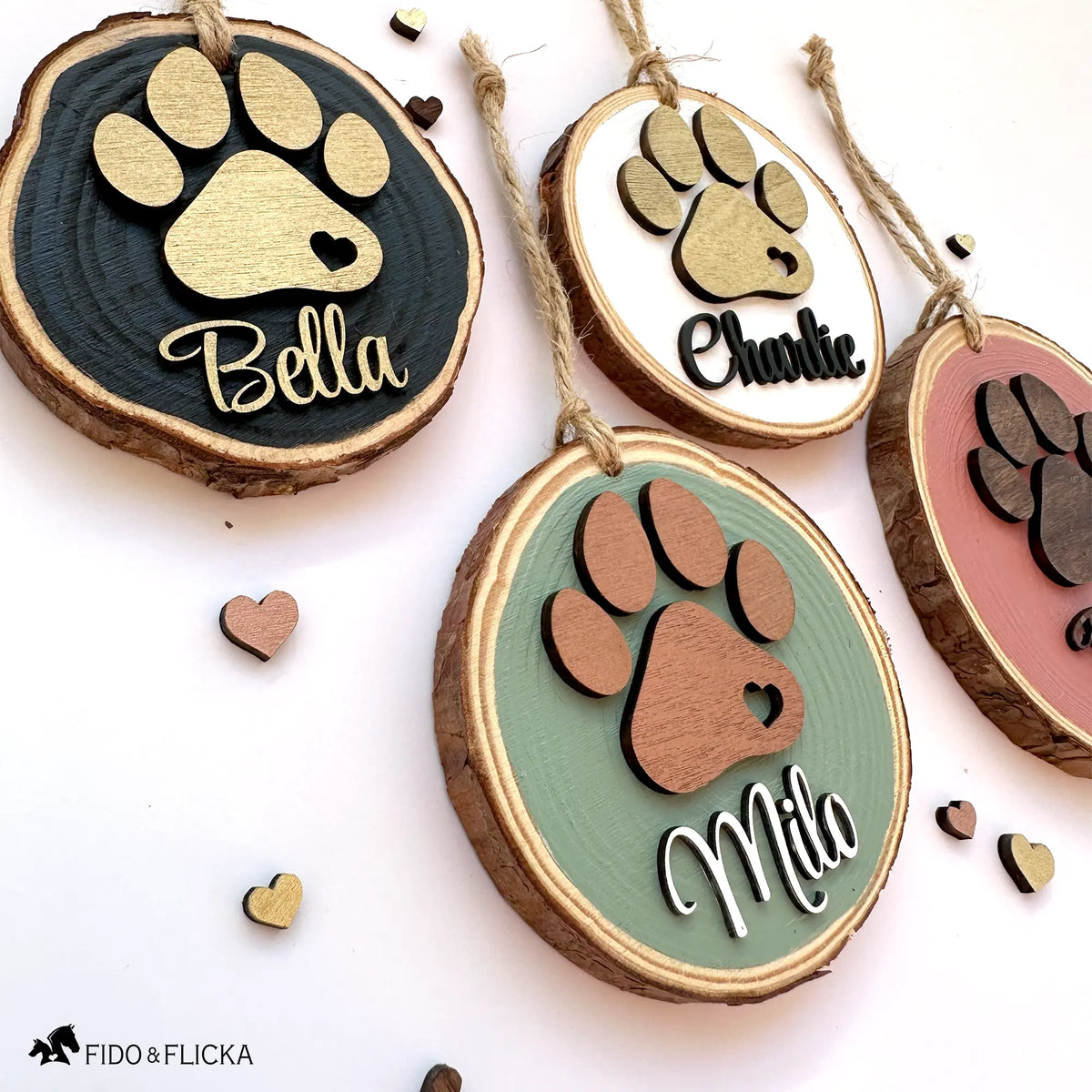 Side-angle view of four personalized wood slice dog ornaments decorated with small wooden heart accents, showing the layered paw prints and name cutouts in various color combinations.