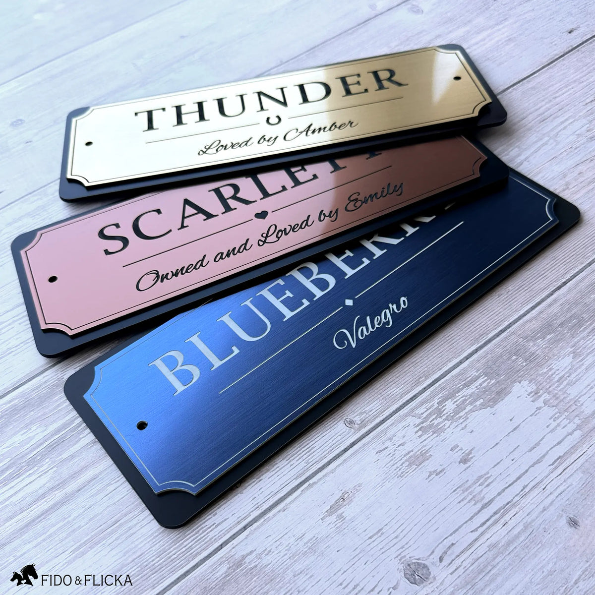 Three personalized horse stall signs in brushed gold, copper, and blue metallic finishes with black acrylic backing, showcasing custom engraved horse name plaques by Fido & Flicka.