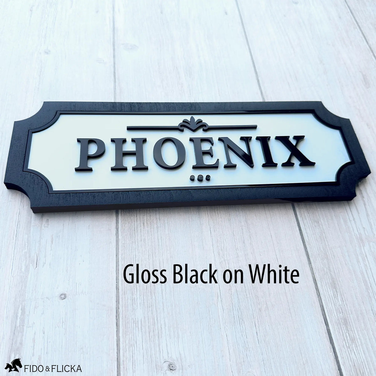 Custom horse stall name plate with raised gloss black acrylic lettering on a white background, framed in black wood and personalized with the name Phoenix.