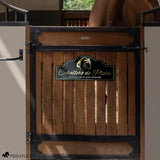 Personalized horse stall sign mounted on a wood and black iron stall door with a chestnut horse visible in the background. The arch-top sign reads 