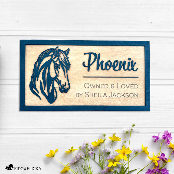 Wooden plaque with horse design and text on a white background with flowers.