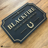 Decorative horse nameplate for stall with 'BLACKFIRE' and a horseshoe on a wooden surface.