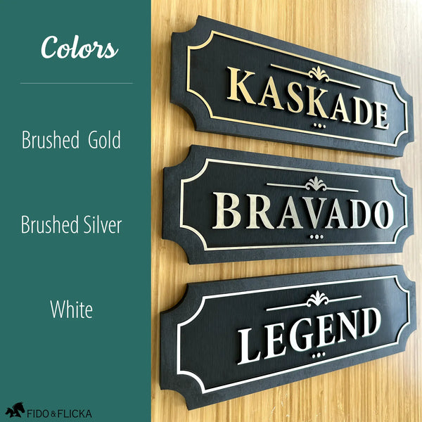 Three personalized horse stall signs showing available color options brushed gold on black reading Kaskade brushed silver on black reading Bravado and white on black reading Legend displayed on warm wood wall by Fido and Flicka