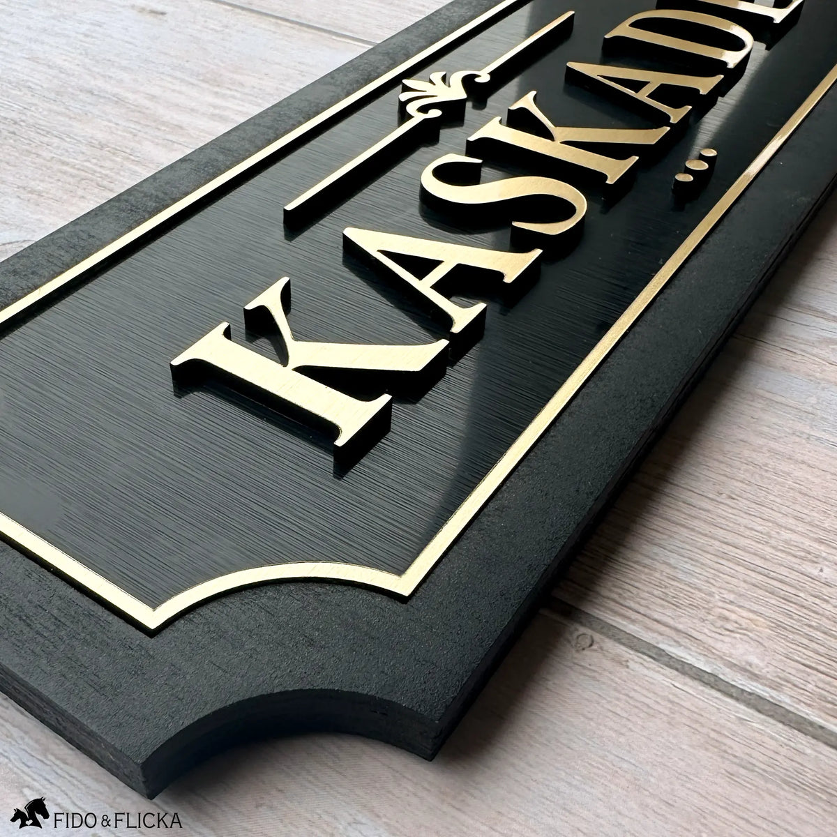 Close up detail of horse stall sign showing raised brushed gold acrylic letters on brushed black acrylic base with sealed black wood frame and backing