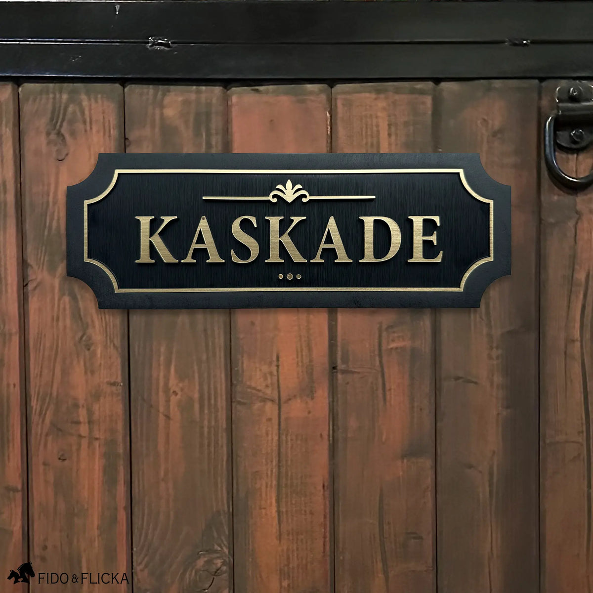 Black and gold layered acrylic and wood horse stall name plate reading ‘Kaskade,’ mounted on a brown wooden stall door with black metal hardware