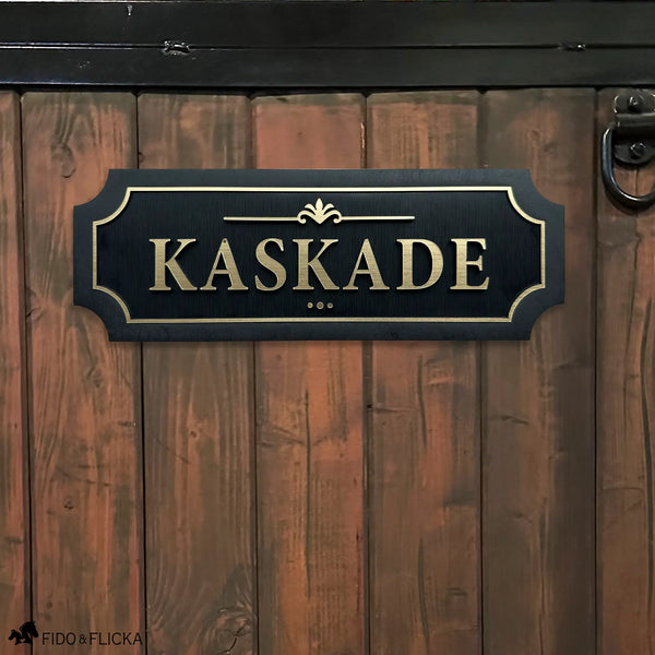 Black and gold layered acrylic and wood horse stall name plate reading ‘Kaskade,’ mounted on a brown wooden stall door with black metal hardware