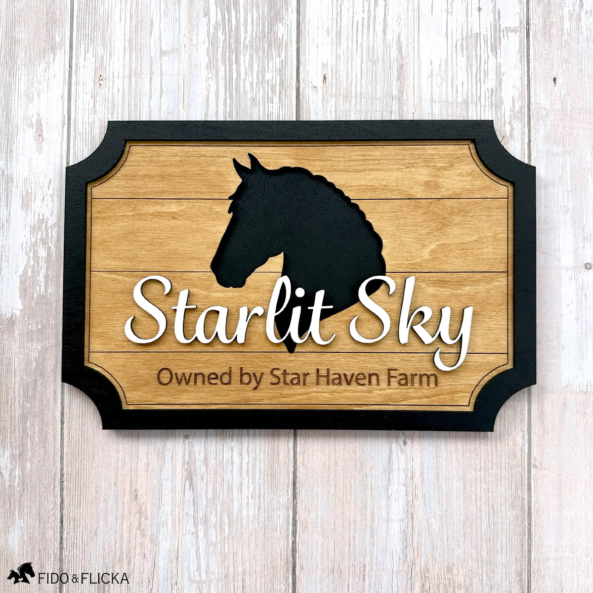 Straight-on view of a personalized wood horse stall sign with a black horse head silhouette, the name ‘Starlit Sky’ in raised script, and ‘Owned by Star Haven Farm’ engraved below