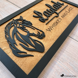 A custom wooden horse stall sign featuring a layered black silhouette of a horse’s head and raised cursive text reading “Laylah,” with “Whiskey and Lace” engraved below. The sign has a natural wood background framed in black, showcasing a handcrafted, personalized design by Fido & Flicka.