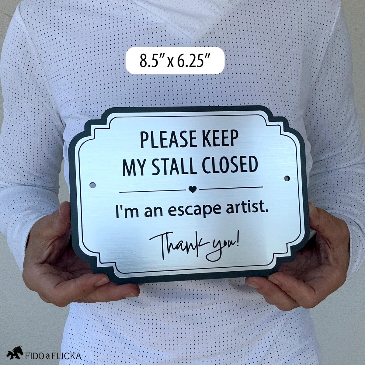 Brushed silver horse stall warning sign reading “Please Keep My Stall Closed, I’m an escape artist,” shown held in two hands for scale, 8.5" x 6.25"