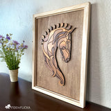 Angled view of a layered wood horse head wall art resting on a dark wooden surface. The framed artwork features intricately cut and stained wooden pieces forming a Baroque-style horse, with a small bouquet of purple and white flowers placed beside it against a textured, light-colored wall.
