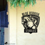 Personalized metal horse barn sign with show jumping horse and rider design, custom stable name ‘Blue Ribbon Stables,’ mounted on equestrian facility wall.