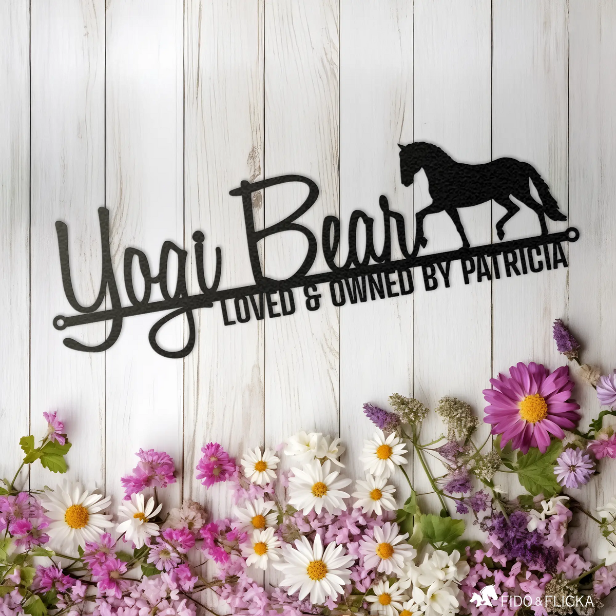 Custom metal horse name sign reading 'Yogi Bear – Loved & Owned by Patricia' with trotting horse silhouette, displayed on white wood background with spring flowers.