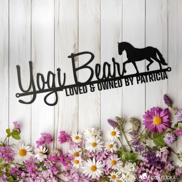 Custom metal horse name sign reading 'Yogi Bear – Loved & Owned by Patricia' with trotting horse silhouette, displayed on white wood background with spring flowers.