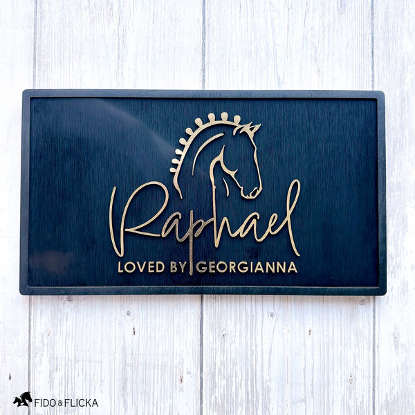 Elegant acrylic and black wood horse stall nameplate featuring a gold silhouette of a braided show horse and the name “Raphael,” with the inscription “Loved by Georgianna.” Custom equestrian sign by Fido & Flicka, modern and personalized design.