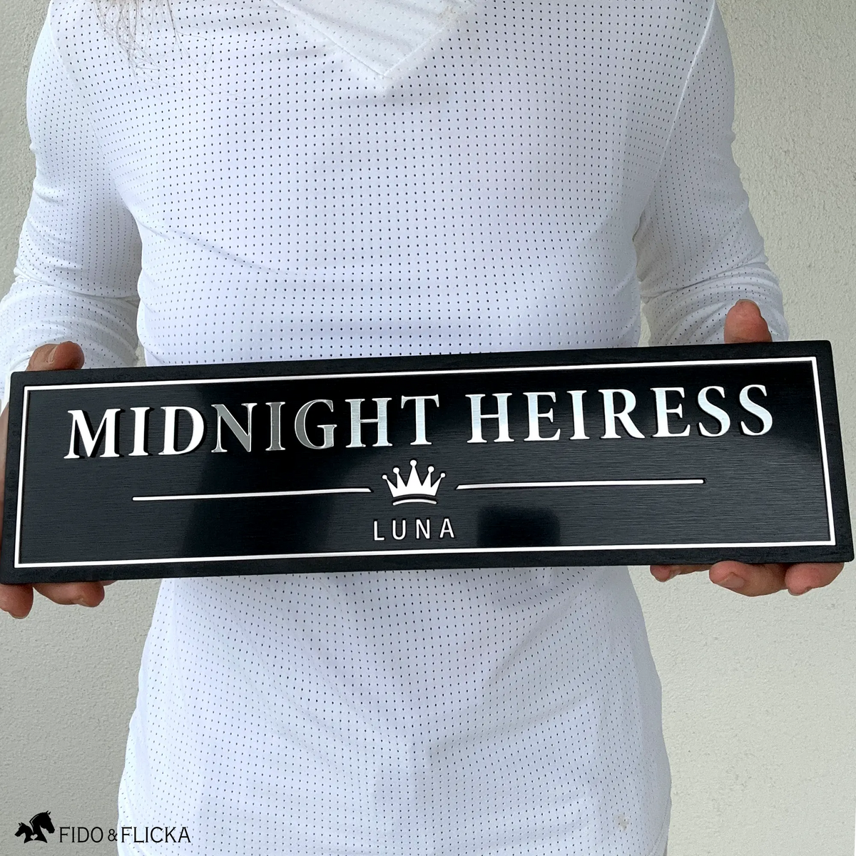 Person holding a 15.5-inch personalized horse stall sign to show the scale and size of the finished black and metallic name plate.