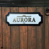 Personalized horse stall sign mounted on a rustic barn door featuring raised gold acrylic lettering, white acrylic backing, and black wood frame.