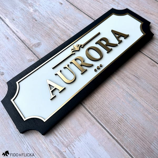 Custom horse stall name plate with raised gold acrylic lettering on a white background and black wood frame, personalized with the name Aurora.