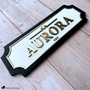 Custom horse stall name plate with raised gold acrylic lettering on a white background and black wood frame, personalized with the name Aurora.