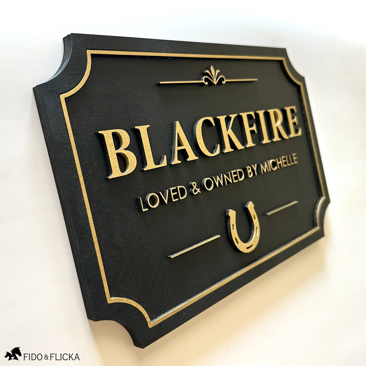 Black and gold horse name stall sign with 'BLACKFIRE' and 'LOVED & OWNED BY MICHELLE' on a white background.