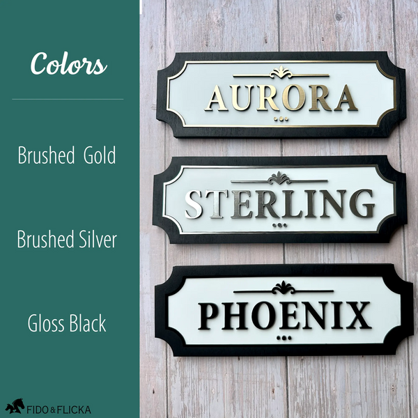 Three personalized horse stall signs on barn wall showing white acrylic color options brushed gold reading Aurora brushed silver reading Sterling and gloss black reading Phoenix with black wood frame by Fido and Flicka