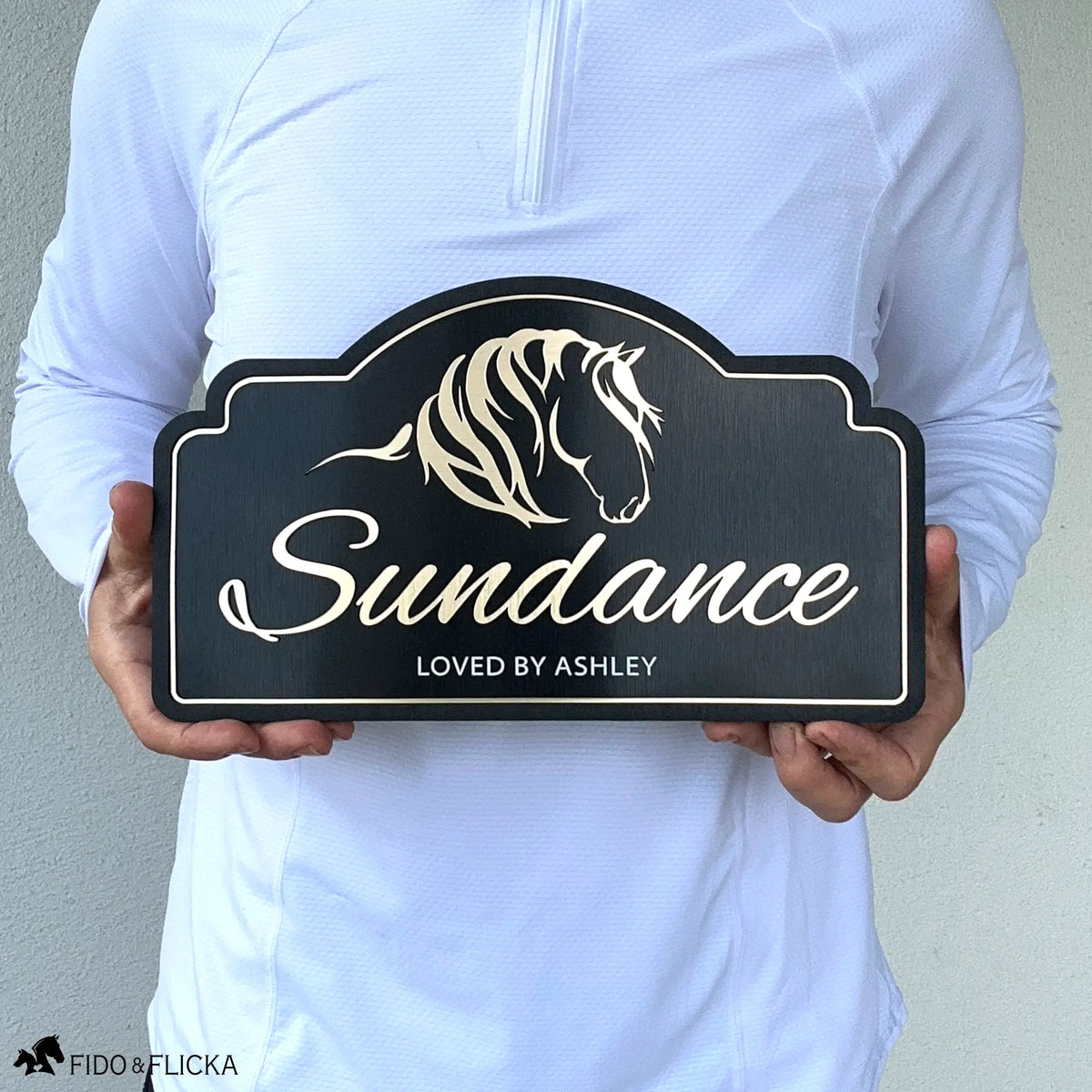 Person holding a personalized horse stall sign featuring layered horse artwork, custom horse name, and engraved text on a black acrylic plaque to show the sign's size and scale.