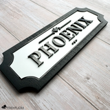 Modern horse stall name plaque with raised black acrylic lettering on a white background and black wood frame, customized with the name Phoenix.