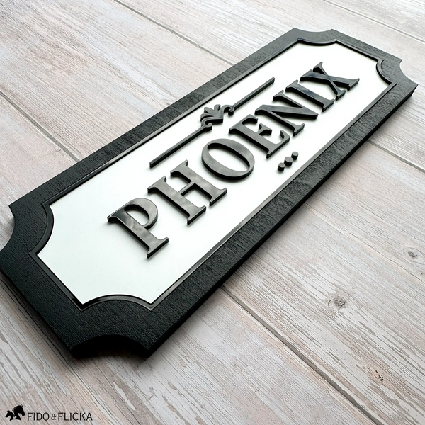 Modern horse stall name plaque with raised black acrylic lettering on a white background and black wood frame, customized with the name Phoenix.