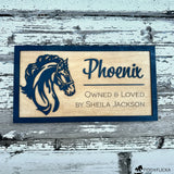 Custom wooden horse stall sign made from Baltic birch. Features layered black horse head silhouette and engraved text “Phoenix, Owned & Loved by Sheila Jackson.” Personalized barn name plate displayed on rustic weathered wood background